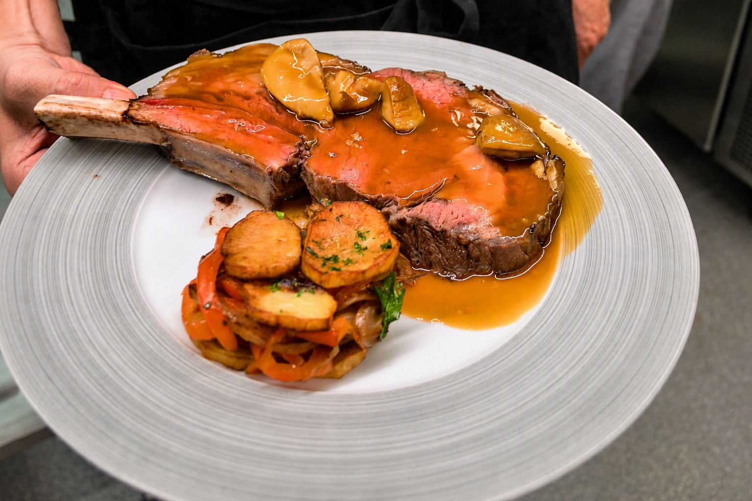 Benet kotelett med blank brun saus, sopp og sprøstekte potetskiver på hvit tallerken