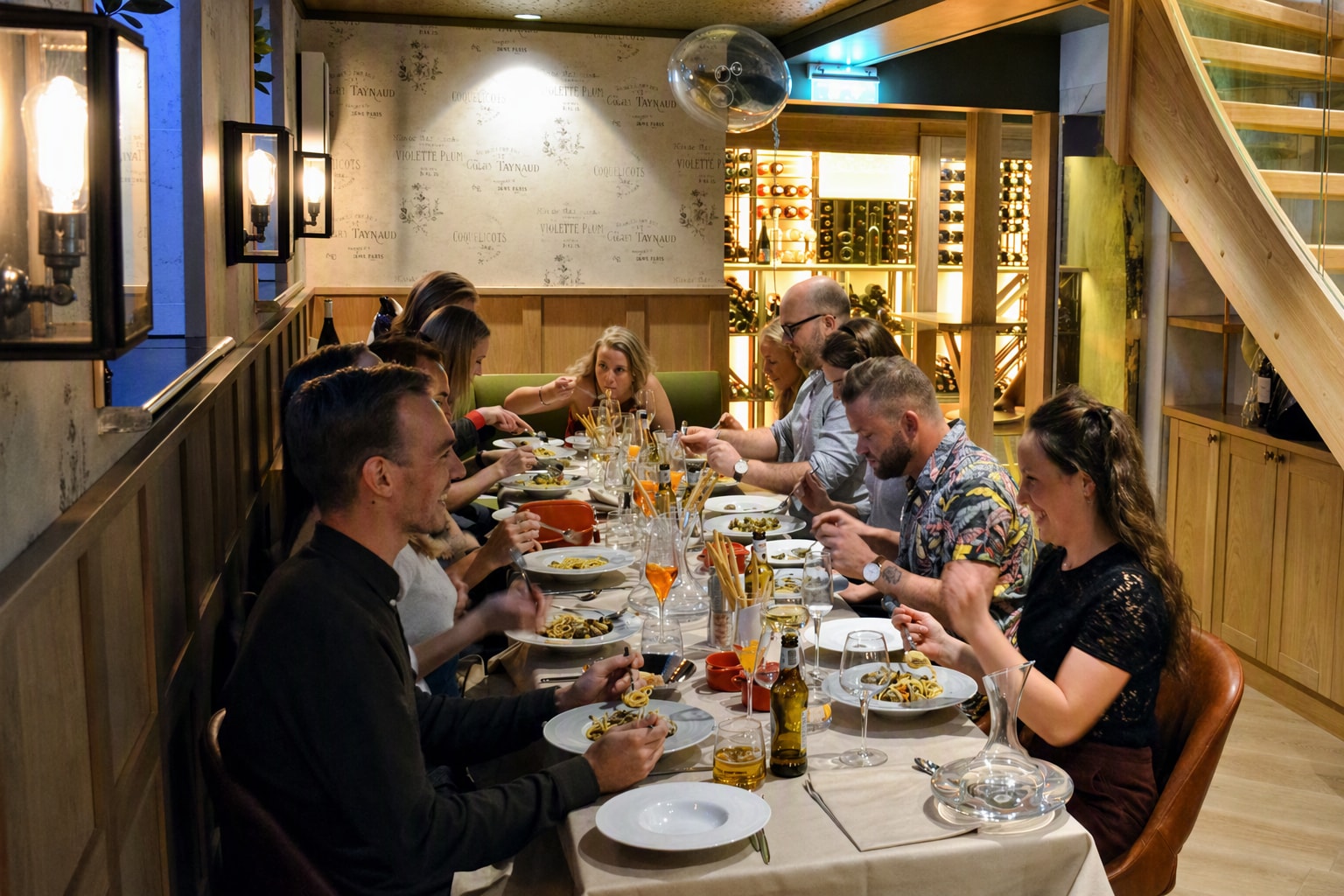 Selskap på tolv gjester rundt ett langt bord med hvite duker i underetasjen, med trappen og vinkjelleren bak